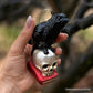 RAVEN ON SKULL AND BOOK GLASS HOLIDAY ORNAMENT